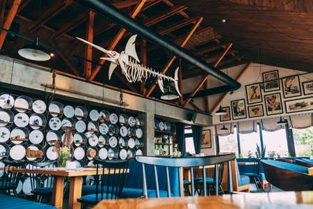ZATOKA, UKRAINE - JUNE 14 2021: Interior of the restaurant's pub is in a modern retro style with a predominance of wood and metal finishes. An artificial fish skeleton hangs on the ceilingのeditorial素材