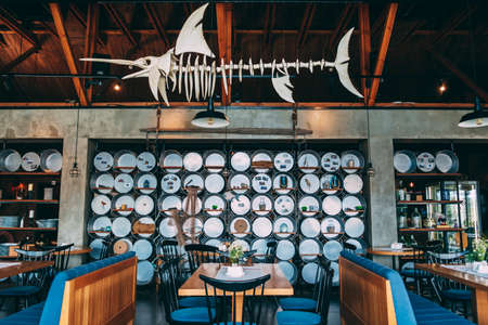 ZATOKA, UKRAINE - JUNE 14 2021: Interior of restaurant is in a modern style with a predominance of wood and metal finishes. There are metal basins on wall and an artificial fish skeleton on ceilingのeditorial素材