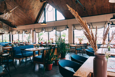 ZATOKA, UKRAINE - JUNE 14 2021: Interior of the restaurant's pub is in a modern retro style with a predominance of wood and metal finishes. Restaurant hall with tables. On floor of a vase of flowersのeditorial素材