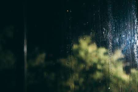 Raindrops on glass at night. Behind the glass trees and a lantern. Abstractionの写真素材