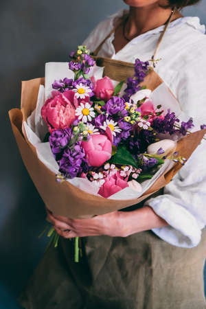 Girl on a dark background stands sideways and holds a bouquet of summer flowers in a paper bag. Florist conceptの写真素材