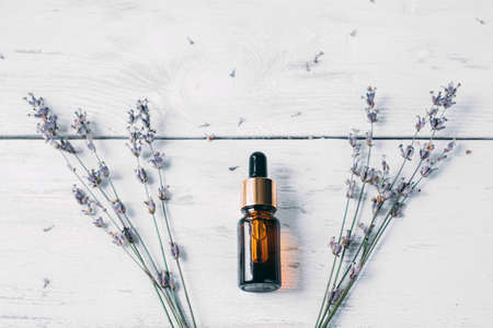 Flat lay composition with lavender flowers and natural lavender oil in brown bottle on white wooden background.の写真素材