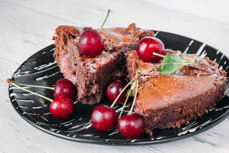 Chocolate brownie on a black plate sprinkled with cherries.