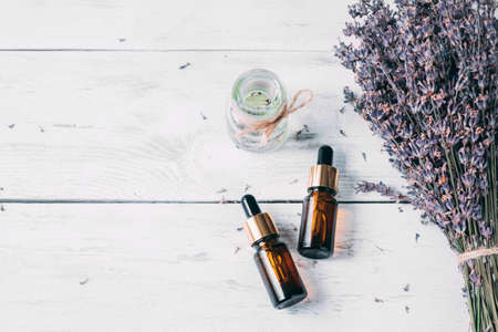 Flat composition with lavender flowers and natural lavender oil in brown bottle on white wooden background. Two brown bottles and a transparent jar.の写真素材