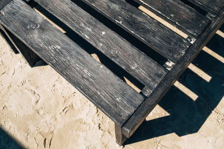 Part of a dark wooden deck chair on the sand.の写真素材