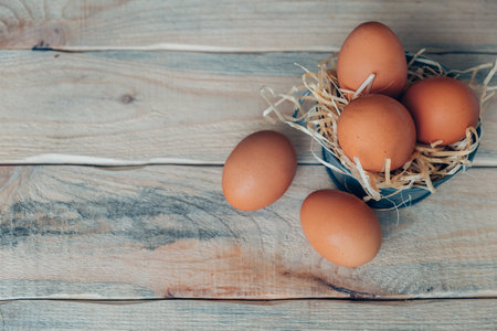 Chicken eggs on decorative straw in a basin on a wooden table.の写真素材