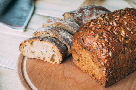 Two different homemade rye breads on a cutting board through the ears. One is cut into slices of...