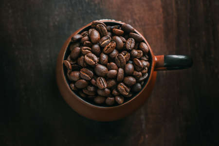 Close-up top view of clay coffee cup filled with roasted coffee beans on wooden table