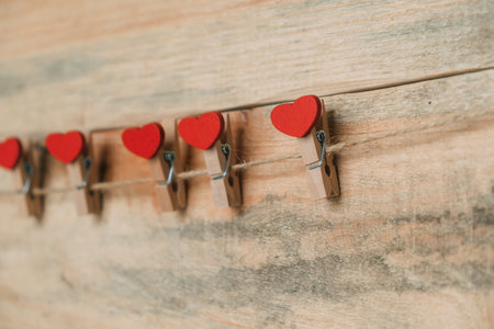 Decorative clothespins with hearts hang on a rope against the background of boards in a row. Valentine's Day.の写真素材