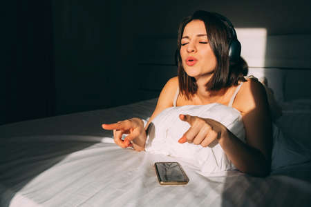 Portrait of a beautiful Caucasian girl listening to her favorite music through headphones in bed....