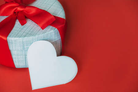 White empty card in shape of heart next to gift box on red background.の写真素材