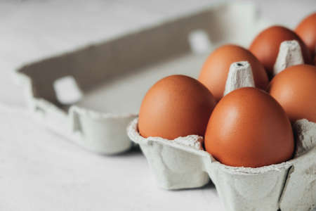 Brown chicken eggs in cardboard tray on white wooden table. Side view of an open container with eggs.の写真素材