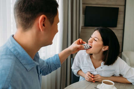 Young couple in love having fun breakfast in the kitchen. Man feed woman cake. Young people have fun in the morning. happy family.の写真素材
