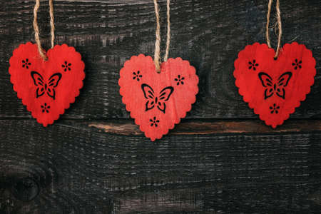 Three wooden hearts close-up hanging on dark wooden background.の写真素材