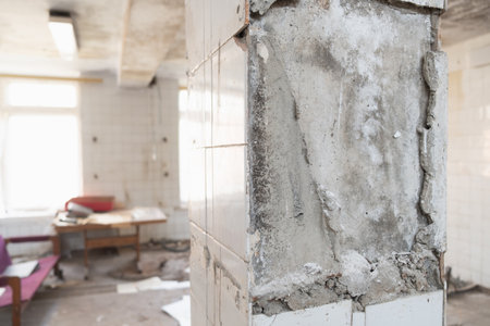 Part of a wall with peeling plaster and tiles in an abandoned room. An old table and chair are visible in the background, creating the atmosphere of an abandoned office or laboratoryの写真素材