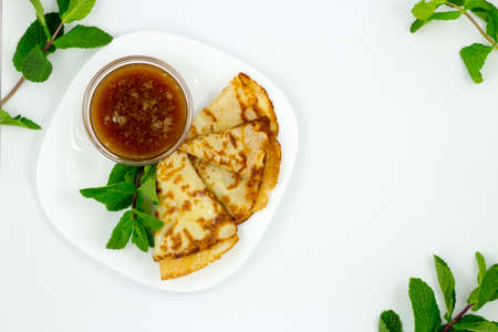 Crepes on a white plate with mint leaves and a Cup of honeyの写真素材