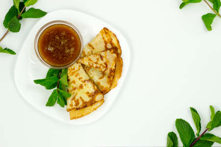 Crepes on a white plate with mint leaves and a Cup of honeyの写真素材