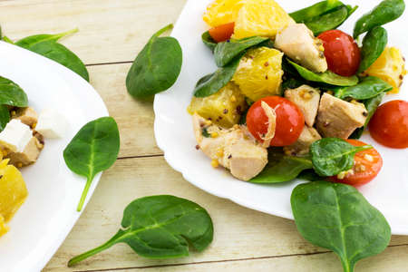 Garnished with cut feta salad from spinach, chicken, cherry tomatoes and orange on white plateの写真素材