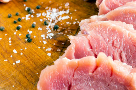 Cut raw pork on wood board with background of salt and black pepperの写真素材