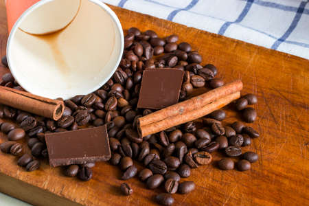 Coffee in orange paper glass with background of coffee beans, chocolate chunks and cinnamon sticksの写真素材