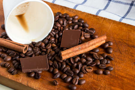 Coffee in white plastic glass with background of coffee beans, chocolate chunks and cinnamon sticks
