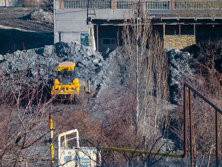 Yellow tractor rakes buckets clay near the plant