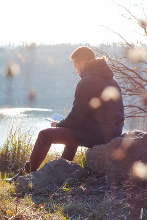 the guy is sitting on a cliff of a career reading a book, on an autumn sunny dayの写真素材