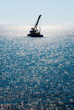 Black silhouette of a floating crane against the background of a blue sea and sky.