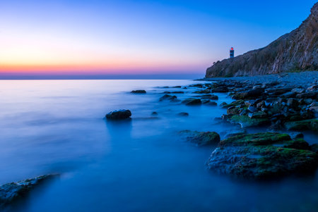 Beautiful seascape with lighthouse at sunset. Mountains and the sea with a long passage.の写真素材