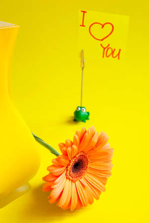 Gerber next to a yellow glass vase on an isolated yellow background and an inscription on a leaflet: "I love you."の写真素材