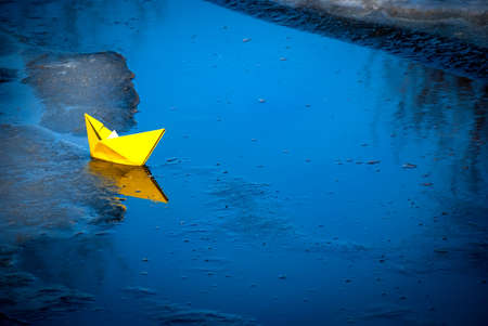 A colorful paper ship sails in the lake. It's got ice and snow around it.の写真素材