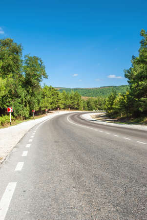 Mountain landscape. Mountain road, going away against the background of a blue sky and pines.の写真素材