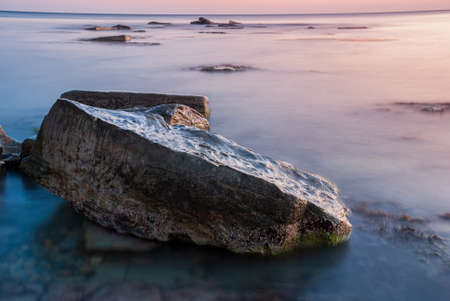 Seascape at sunset. Sea on a long shutter with stones and rocks.の写真素材