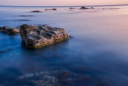 Seascape at sunset. Sea on a long shutter with stones and rocks.の写真素材