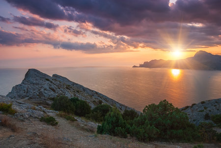 Sudak, Crimea - a view from Cape Meganom. Sunset sky with beautiful clouds. The Black Sea and the ridge of the Crimean mountains in the rays of the evening sun.の写真素材