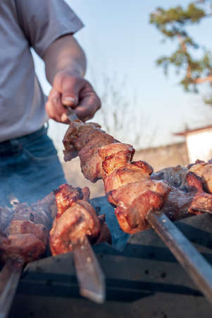 A man prepares barbecue on skewers in the grill with smoke.