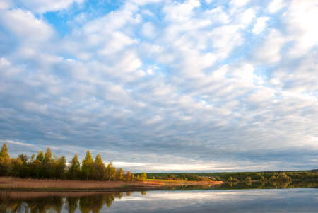 Autumn landscape with lake, trees with yellow leaves and sky with beautiful clouds.