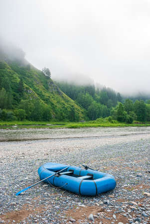 An inflatable blue boat against the background of a mountain landscape in the early morning on the river. Mountains, river, sandbank and pine forest.の写真素材