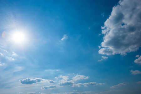 Beautiful, blue summer sky with fluffy clouds and bright sun as a backgroundの写真素材