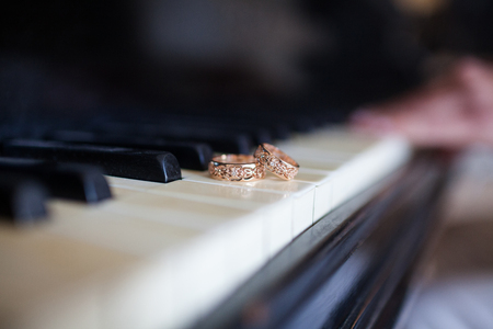 A pair of wedding rings are on the keys of the black piano. In the background in the blur a female hand is discernible, lying on the keys.の写真素材