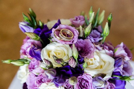 A pair of wedding gold rings on a bouquet of colorful flowers, close up shotの写真素材