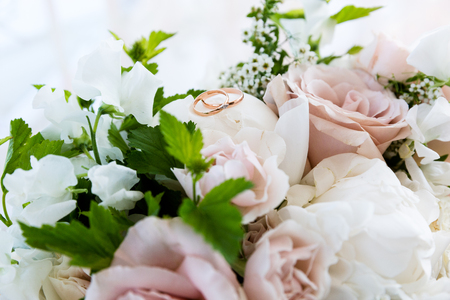 A pair of wedding gold rings on a bouquet of colorful flowers, close up shotの写真素材