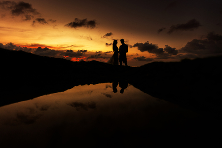Bride and groom on the beach at sunset, their silhouettes are reflected in the sea water.の写真素材