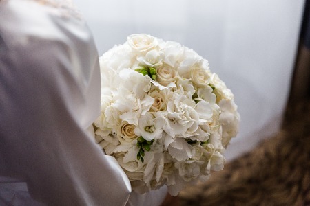 Exquisite bridal bouquet of white flowers of roses, hydrangeas and freesia in the handsの写真素材