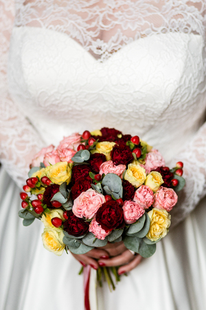 Luxurious bouquet of pink, red and yellow roses in the hands of an unrecognizable brideの写真素材