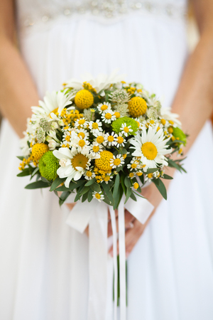 Romantic bouquet of daisies in the hands of an unrecognizable brideの写真素材