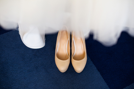 Cream womens shoes on a blue carpet, in the foreground a blurred hem of a wedding dressの写真素材