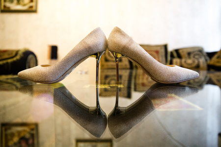 Cream shiny high-heeled shoes on the mirror surface of the tableの写真素材