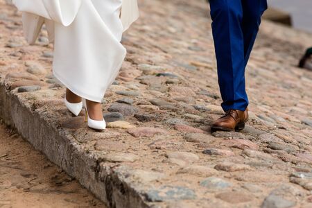 The legs of the groom in brown shoes and the bride in white heels for a walk.の写真素材