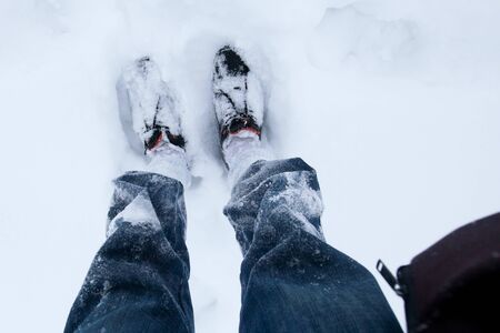 Mans legs in blue jeans and black shoes outdoors in the snow